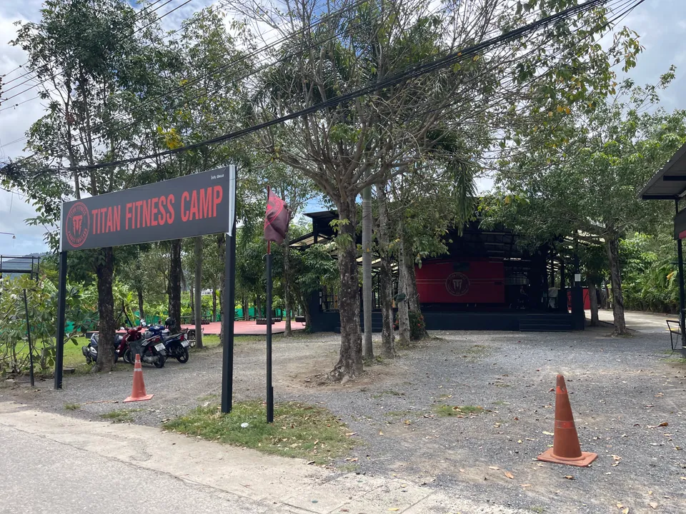 Titan Fitness Camp sign and its open-sided training hall among trees on Soi Taied